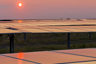 intense red orange sun above the horizon reflecting warm colors across a field of solar panels in the foreground