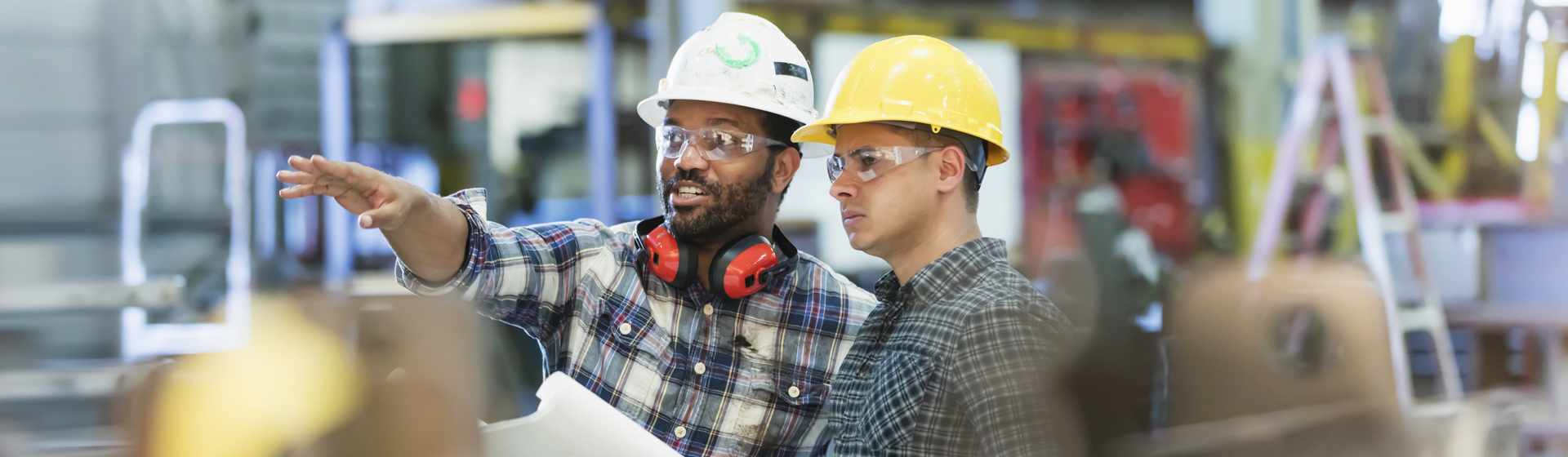 workers talking in a metal fabrication plant wearing hardhats and protective eyewear