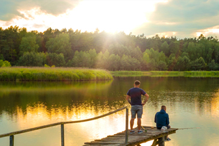 boys on wooden pier overlooking lake with sunburst above treeline