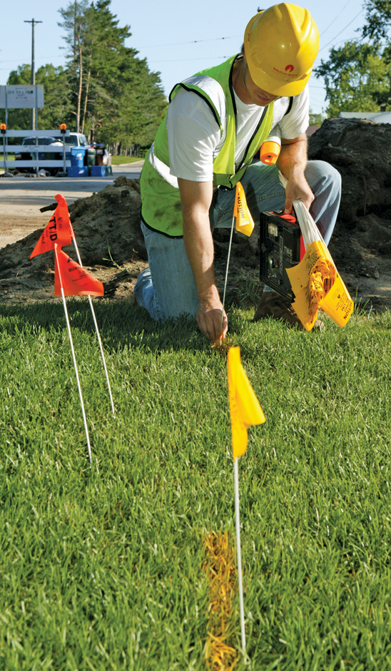 employee placing facility flag markers on to lawn along with spray paint marking